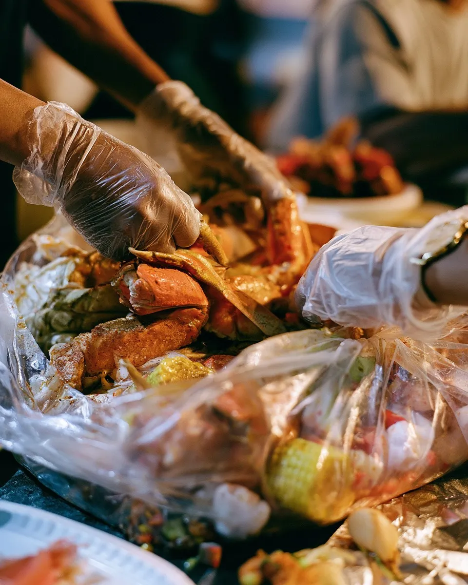 Gloved hands cracking crab legs over a boil bag